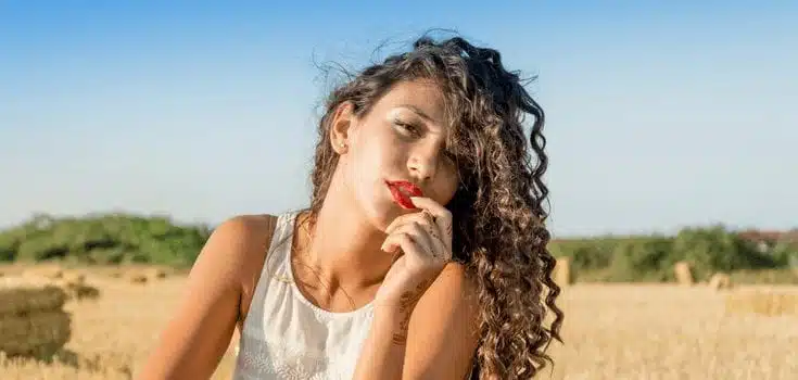 moça com cabelo crespo sentada em um campo ao sol